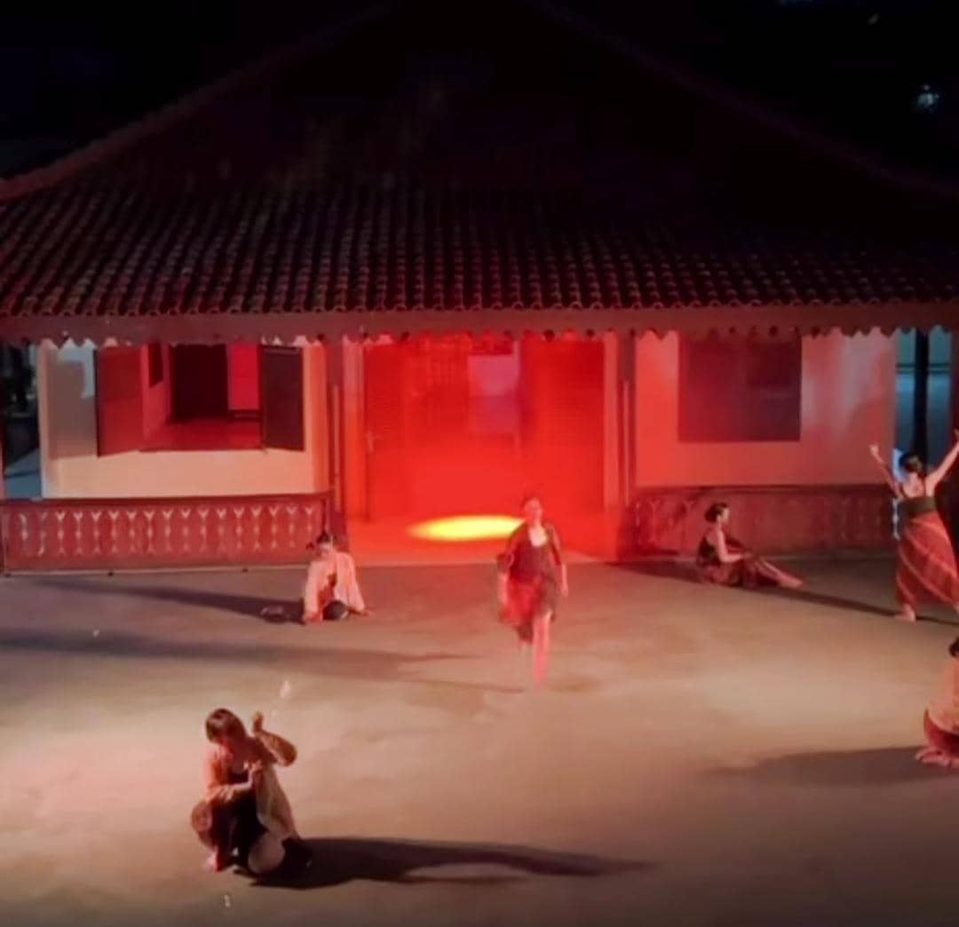 Beberapa penari menampilkan pertunjukan tari di halaman bangunan tradisional dengan pencahayaan merah yang dramatis pada malam hari.
