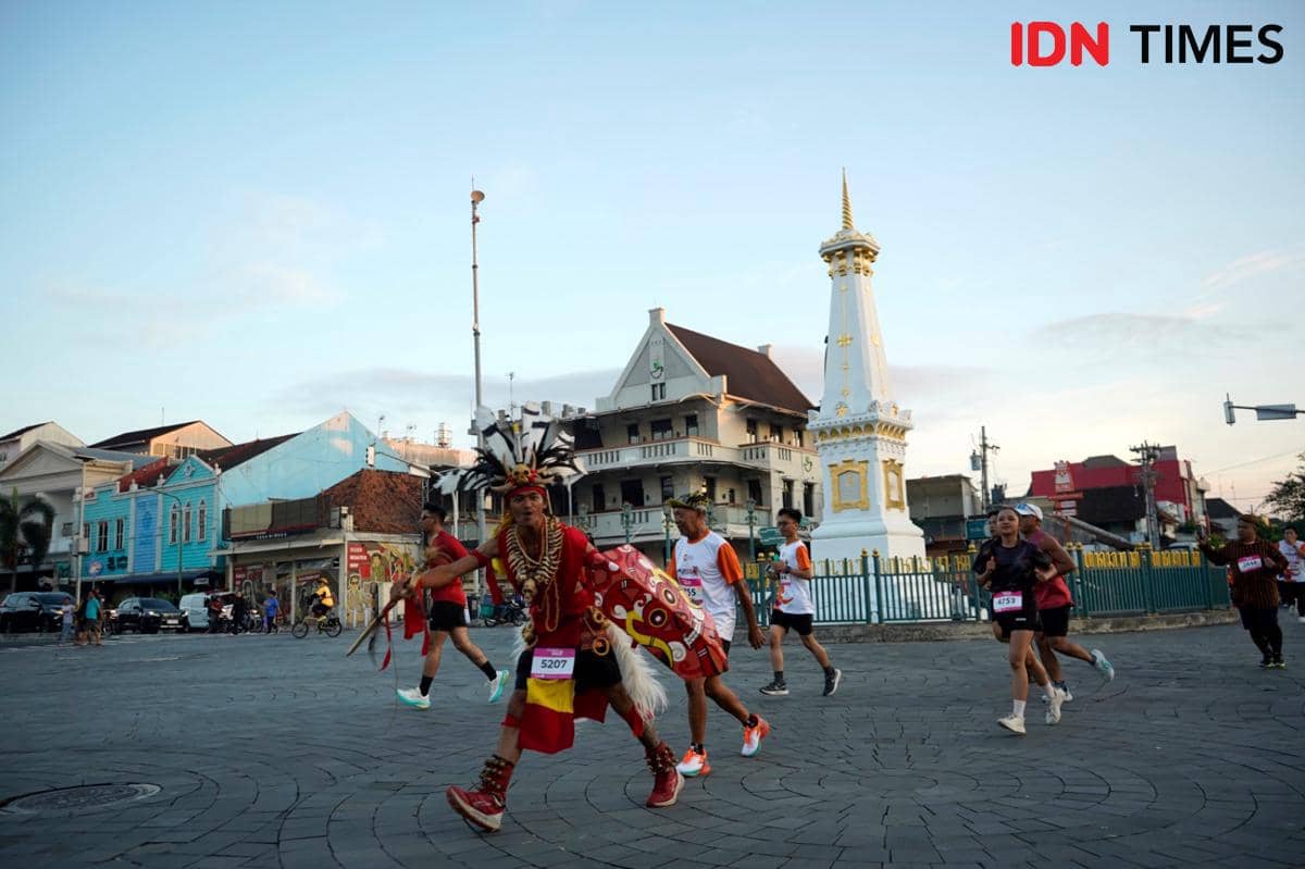 Peserta Jogja Run D-City berlari melewati Tugu Yogyakarta, termasuk seorang peserta dengan kostum tradisional berwarna merah.