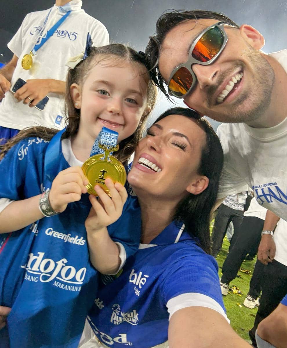 Seorang wanita, pria, dan anak kecil mengenakan jersey Persib Bandung tersenyum sambil memegang medali emas di lapangan.