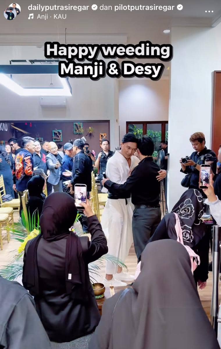 Suasana pernikahan dengan tamu yang mengenakan pakaian formal, beberapa orang mengambil foto dan video di dalam ruangan yang dihias sederhana.