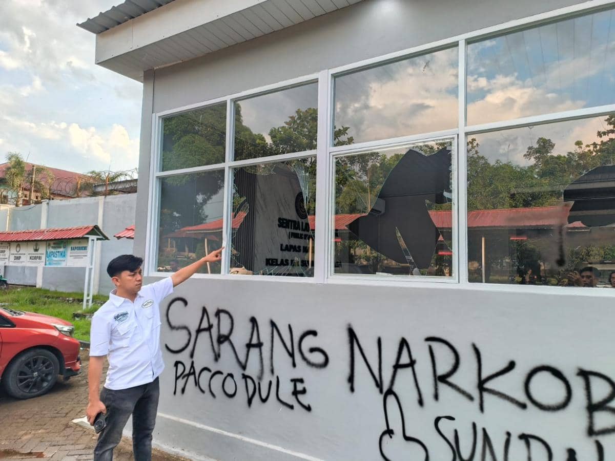 Petugas Lapas Kelas II A Bollangi menunjuk jendela gedung yang pecah dengan dinding bertuliskan grafiti hitam setelah aksi massa.