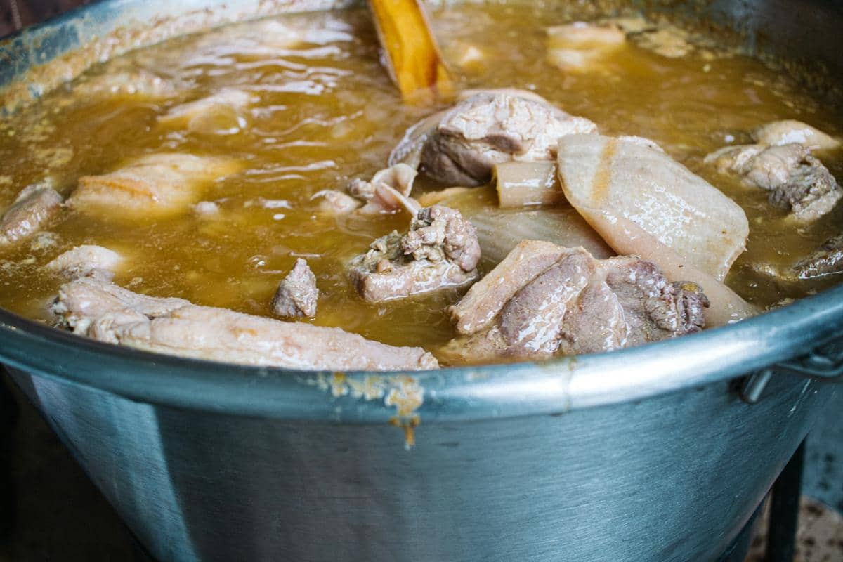 Pot besar berisi potongan ayam yang sedang direbus dalam kuah berwarna kecokelatan dengan sendok kayu di dalamnya.