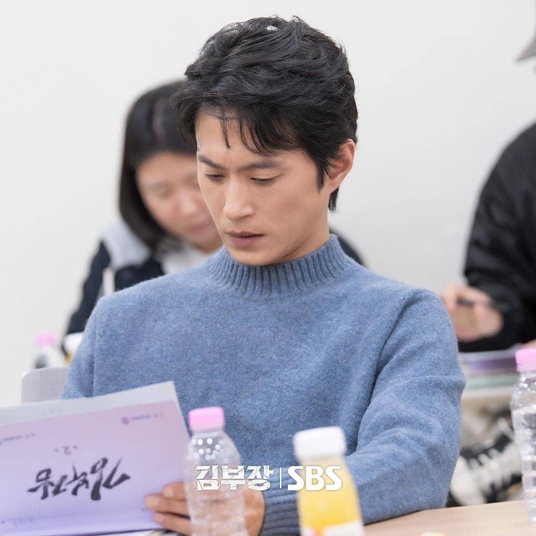 Seorang aktor mengenakan sweter biru sedang membaca naskah di ruang latihan drama Agent Kim Reactivated produksi SBS.