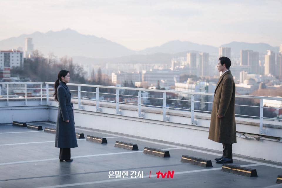 Dua orang berdiri saling berhadapan di atap gedung dengan latar belakang kota dan pegunungan pada cuplikan drama Korea Filing for Love.