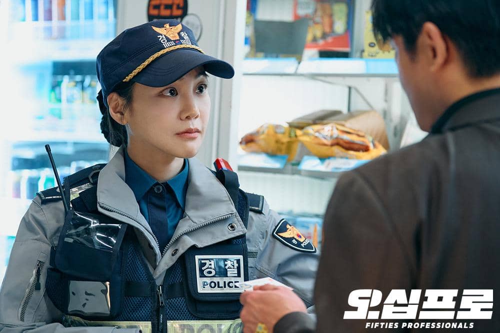 Seorang petugas polisi wanita berbicara dengan seorang pria di dalam toko, mengenakan seragam lengkap dengan rompi dan topi polisi.