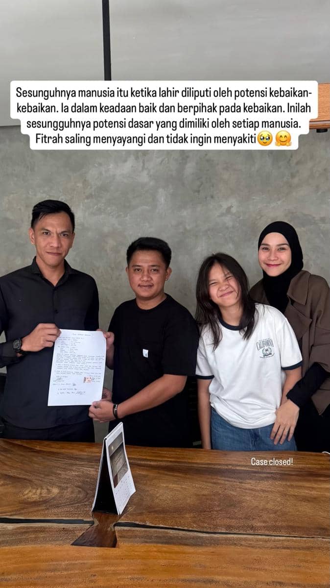 Empat orang berdiri di belakang meja kayu, dua di antaranya memegang dokumen perjanjian yang telah ditandatangani dengan ekspresi ramah.