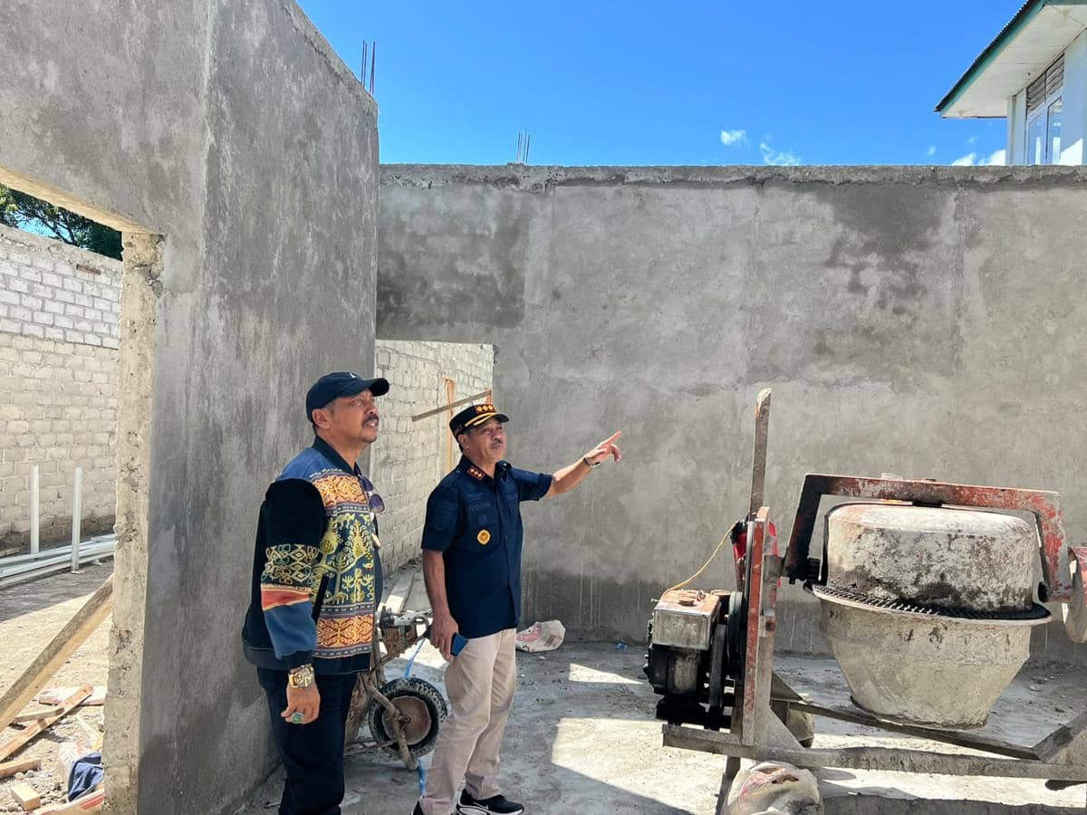 Dua petugas Ditjenpas NTT meninjau pembangunan dapur MBG di Lapas Waingapu, Sumba Timur, dengan dinding beton setengah jadi di bawah langit cerah.