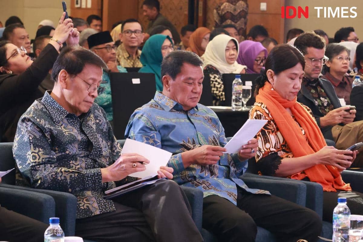 Sejumlah peserta duduk di kursi barisan depan mengenakan batik dan membaca dokumen dalam sebuah acara resmi di ruangan konferensi.