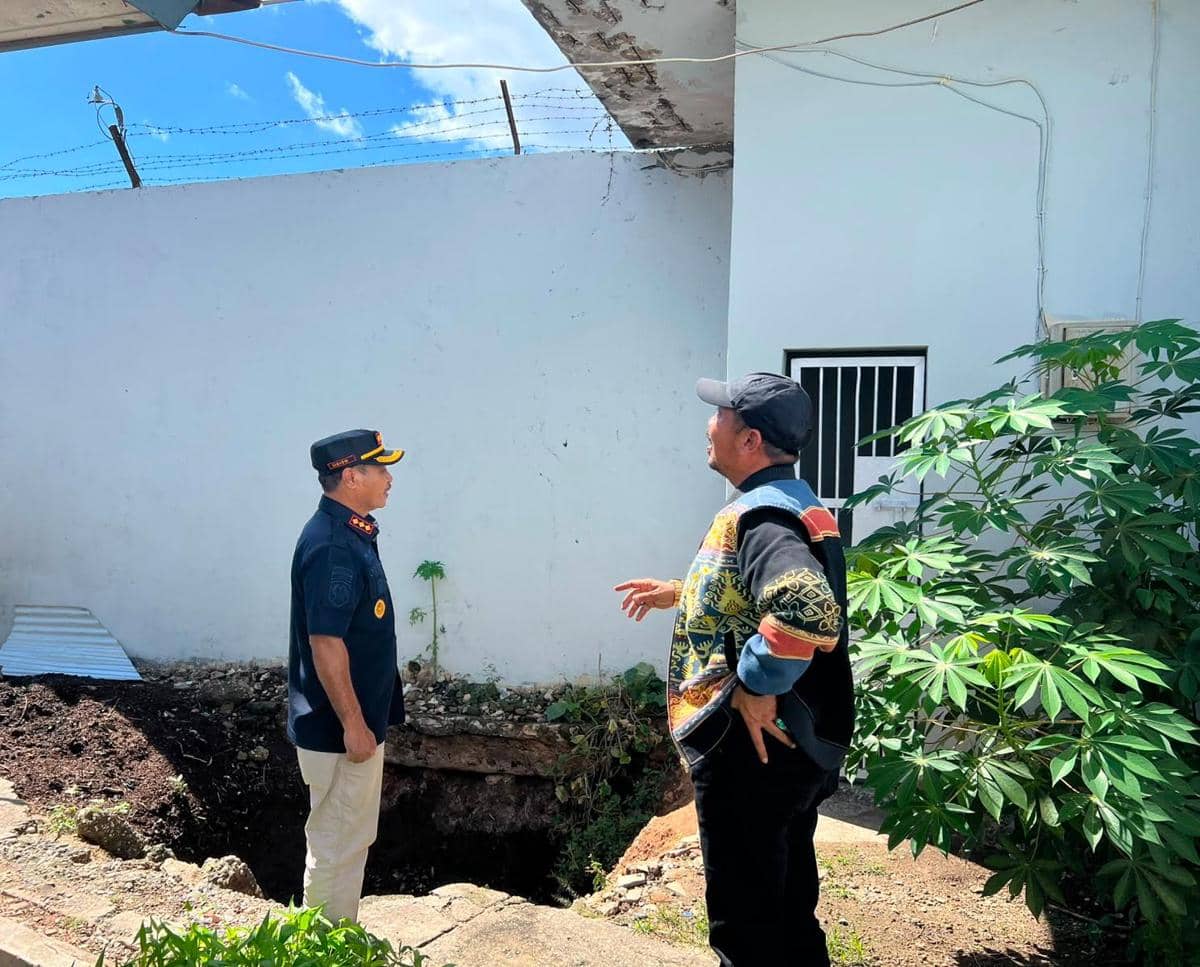 Dua pria berdiskusi di area pembangunan dapur MBG di Lapas Waingapu, Sumba Timur, NTT, dengan latar dinding putih dan langit cerah.