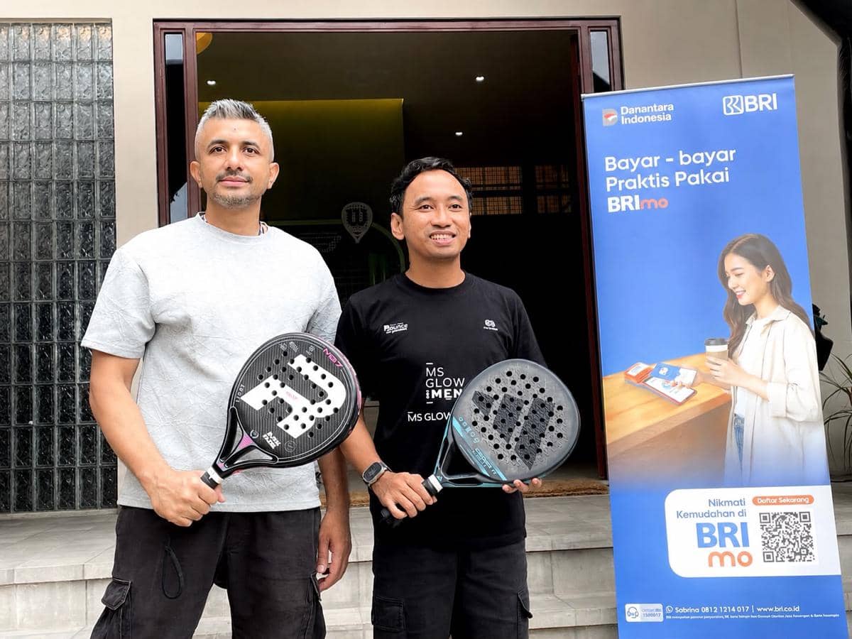 Dua pria memegang raket padel berdiri di depan spanduk BRImo pada acara MS Glow For Men Future Junior Championships di Jakarta.
