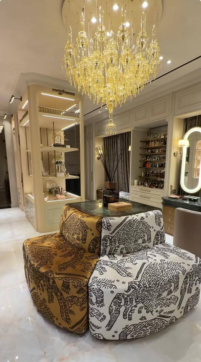 Ruang tamu mewah dengan sofa bermotif hewan, meja kaca, dan lampu gantung kristal besar berwarna emas di langit-langit.