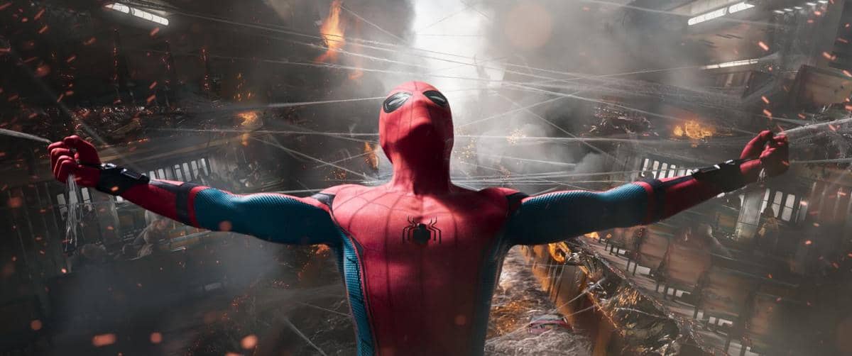 Spider-Man mengenakan kostum merah biru membentangkan jaring laba-laba di tengah kobaran api dan reruntuhan bangunan yang hancur.