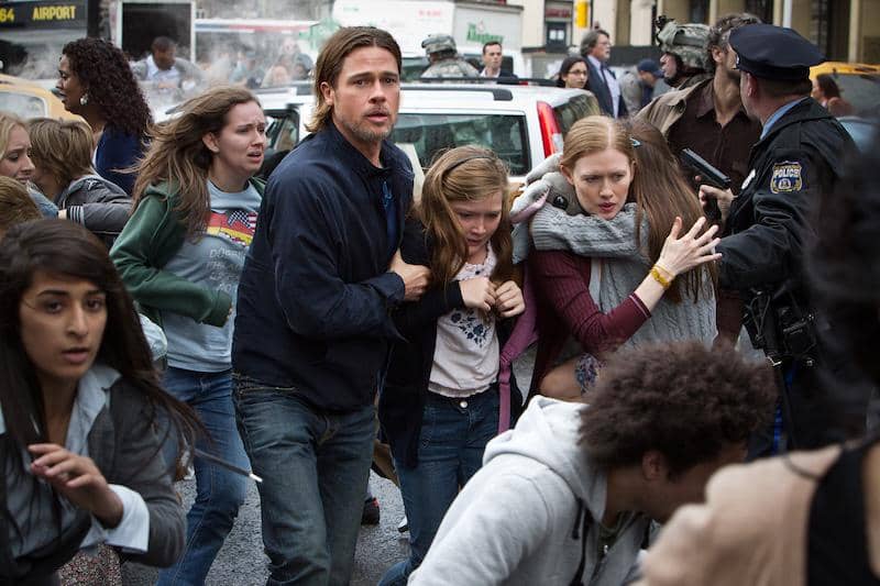 Seorang pria melindungi keluarganya di tengah kerumunan orang yang panik di jalan kota dalam adegan film World War Z.