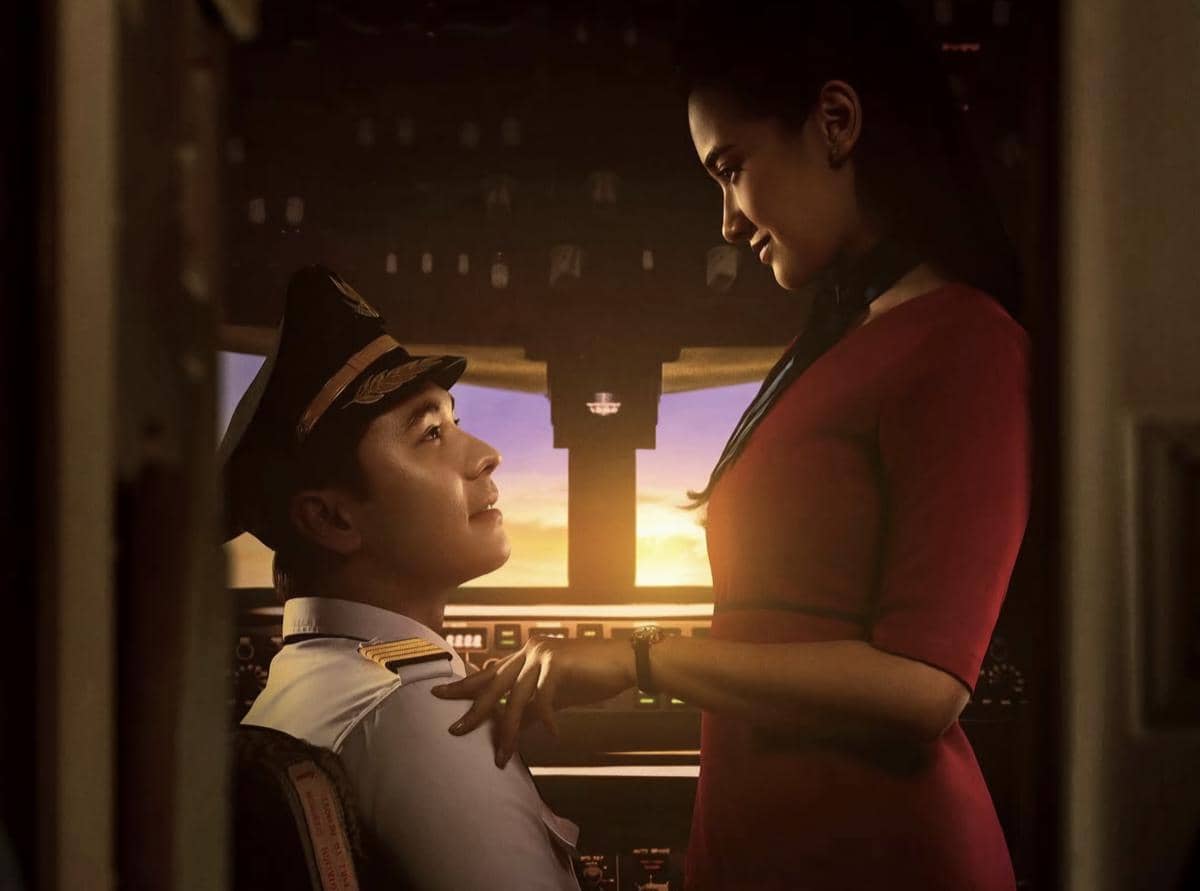 Seorang pilot dan pramugari saling menatap dengan latar kokpit pesawat saat matahari terbenam dalam adegan film Penerbangan Terakhir.
