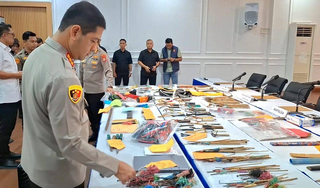 Seorang perwira polisi memeriksa berbagai barang bukti seperti anak panah busur dan senjata tajam yang disita di meja ruang rapat.