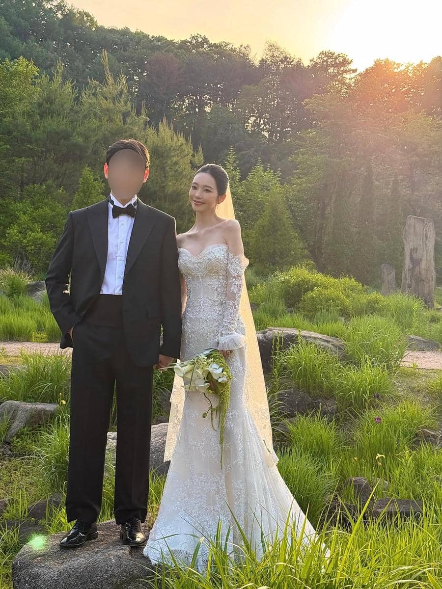 Sepasang calon pengantin berpose di luar ruangan saat matahari terbenam, mengenakan gaun pengantin putih dan setelan jas hitam.