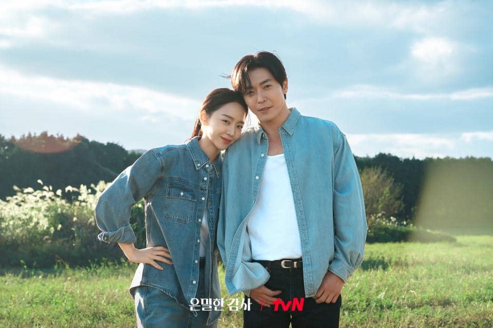 Dua pemeran utama drama Korea Filing for Love berdiri berdekatan di ladang hijau dengan latar langit cerah dan suasana hangat.