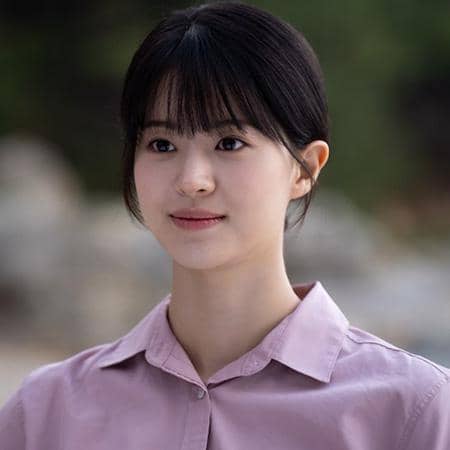 Seorang perempuan berambut hitam dengan poni mengenakan kemeja ungu muda tampak tersenyum lembut di adegan drama The Legend of Kitchen Soldier.