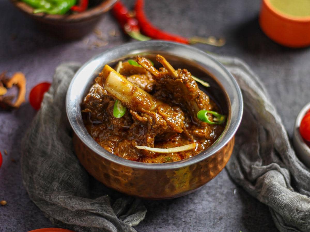 Semangkuk gulai daging berkuah kental disajikan dalam mangkuk tembaga dengan potongan cabai hijau dan rempah di atas meja.