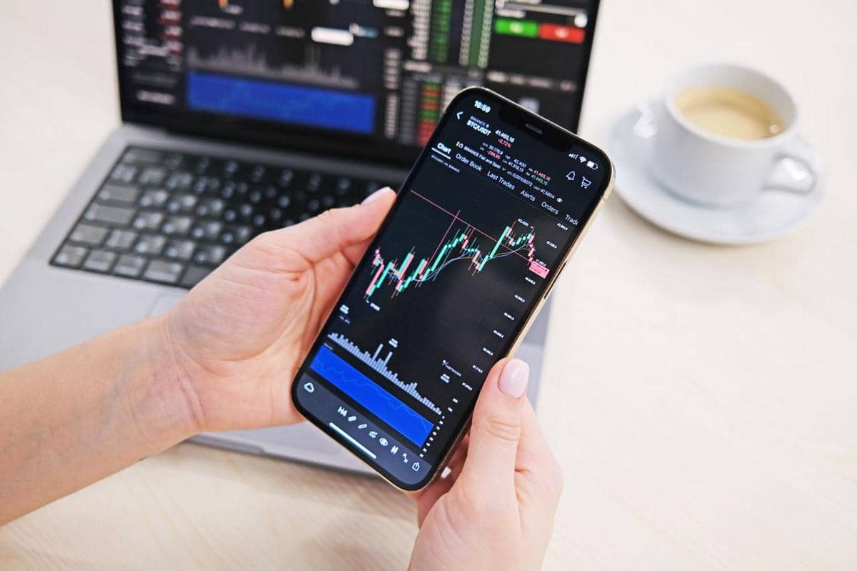 ilustrasi seseorang memegang ponsel yang menampilkan grafik saham