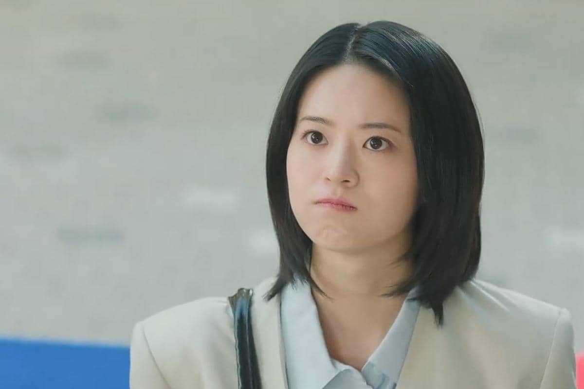 Seorang wanita berambut pendek mengenakan blazer krem dan kemeja biru muda dengan ekspresi wajah kesal dalam cuplikan drama The Legend of Kitchen Soldier.