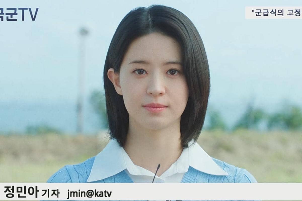 Seorang wanita berambut pendek mengenakan kemeja putih dan sweater biru muda berdiri di luar ruangan dalam cuplikan drama The Legend of Kitchen Soldier.