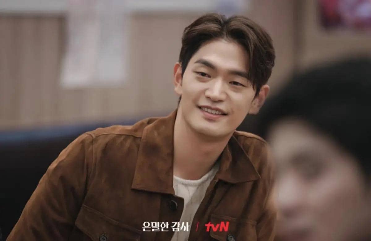 Seorang pria tersenyum mengenakan jaket cokelat dalam adegan drama Korea Filing for Love produksi tvN.