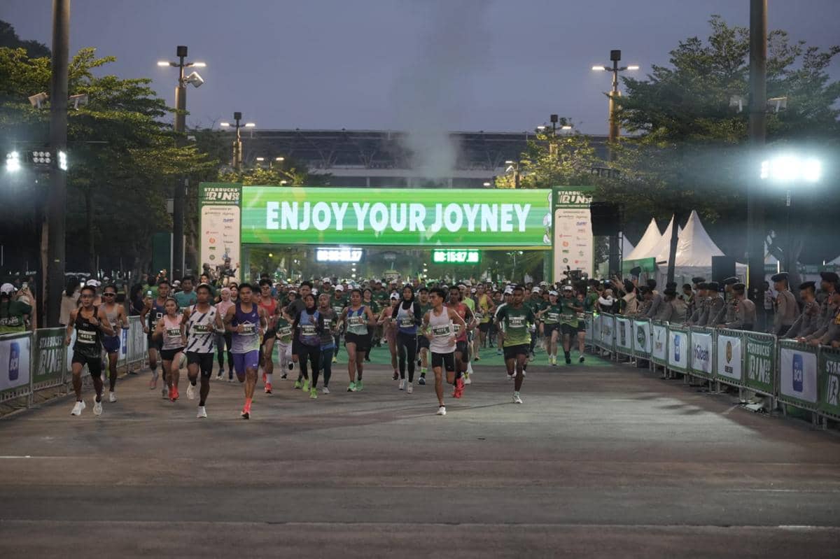 Para pelari memulai lomba lari Starbucks Run 2026 di Jakarta dengan latar belakang papan besar bertuliskan 'Enjoy Your Joyney'.