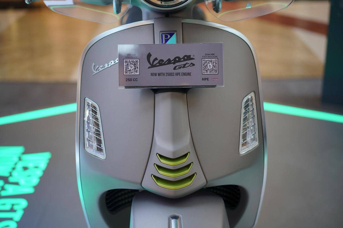 Bagian depan skuter Vespa GTS berwarna abu-abu dengan label informasi mesin 250cc HPE dan logo Vespa di bodi depan.
