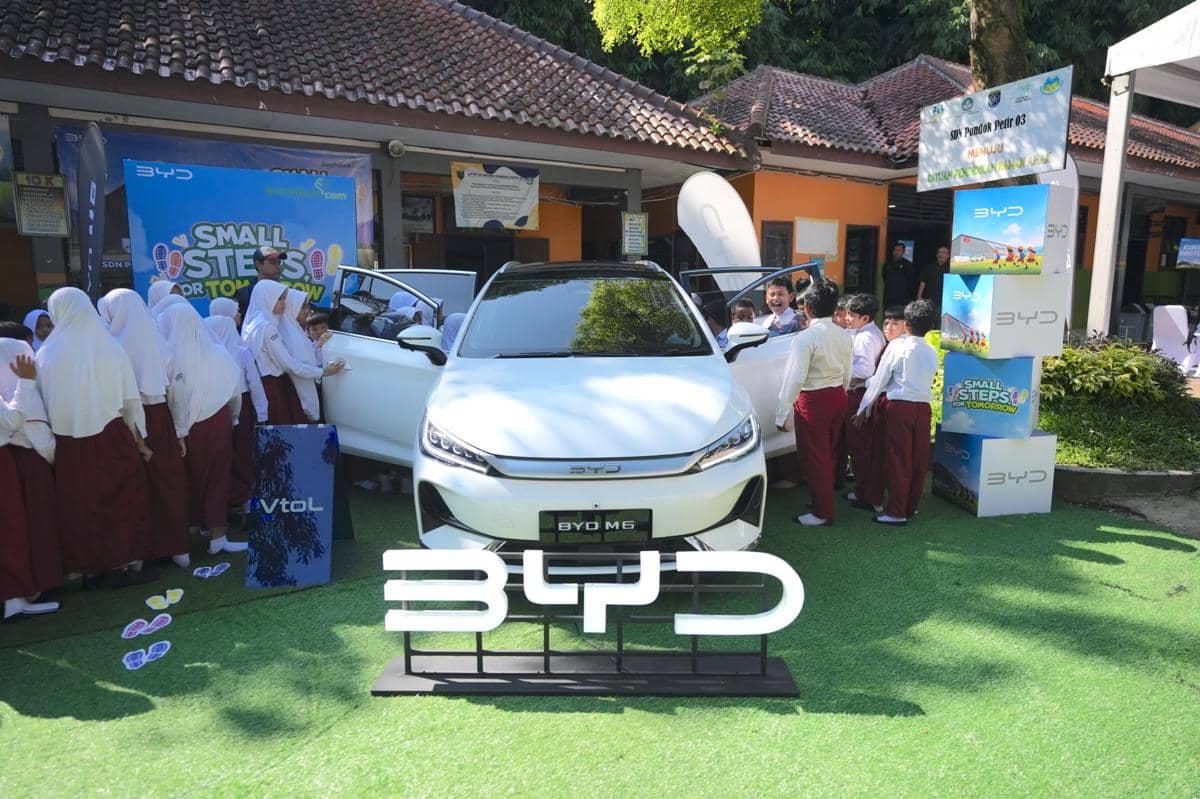 Mobil BYD M6 berwarna putih dipamerkan di sekolah dasar dengan siswa berseragam merah putih yang antusias melihat interior mobil.