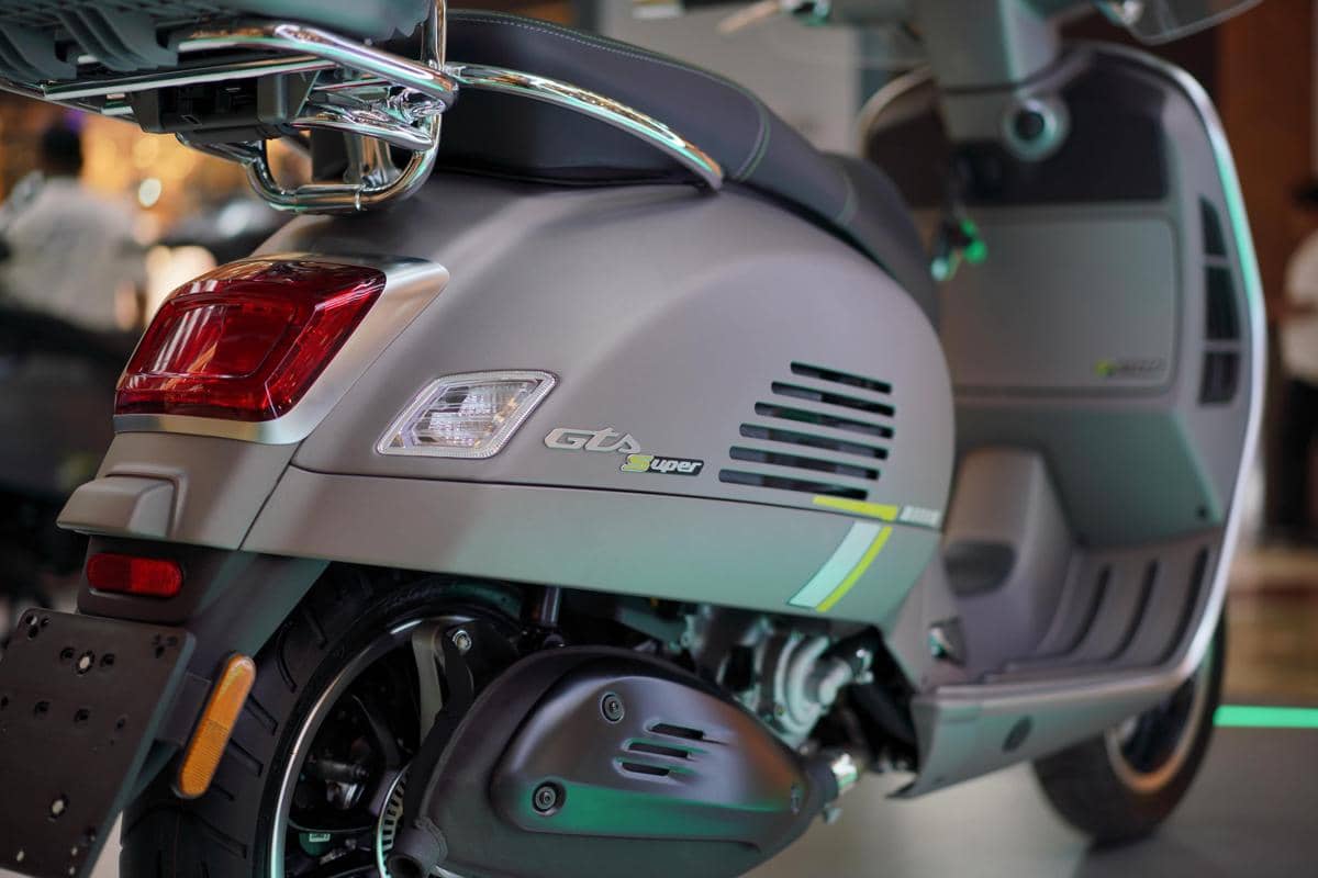 Tampak dekat bagian belakang skuter Vespa GTS Super berwarna abu-abu dengan mesin 250 cc dan desain modern elegan.