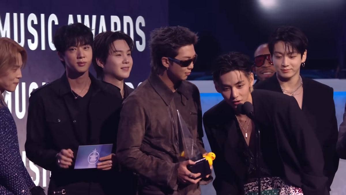 Grup musik asal Korea Selatan berdiri di panggung American Music Awards 2026 sambil memegang piala penghargaan dan berbicara di mikrofon.