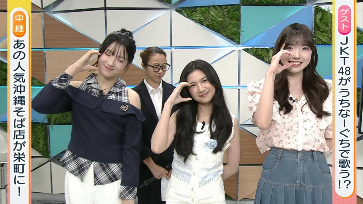 Tiga perempuan tersenyum dan berpose dengan tangan membentuk hati di acara televisi Jepang CATCHY, dengan latar studio berwarna cerah.