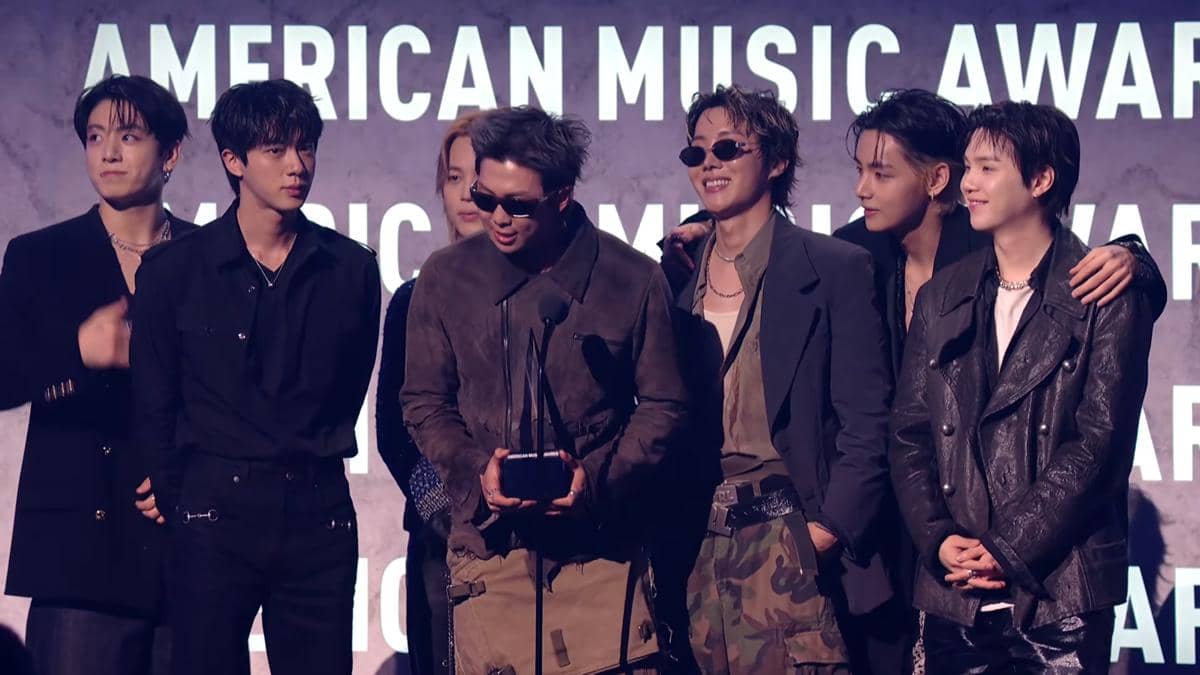 Grup musik asal Korea Selatan berdiri di panggung American Music Awards 2026 sambil memegang trofi penghargaan.