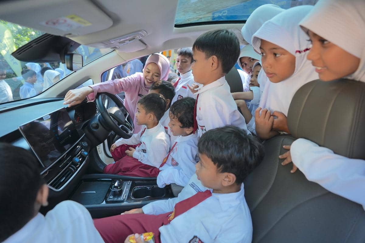 Sekelompok siswa sekolah dasar mengenakan seragam putih merah antusias melihat interior mobil BYD M6 bersama seorang guru.