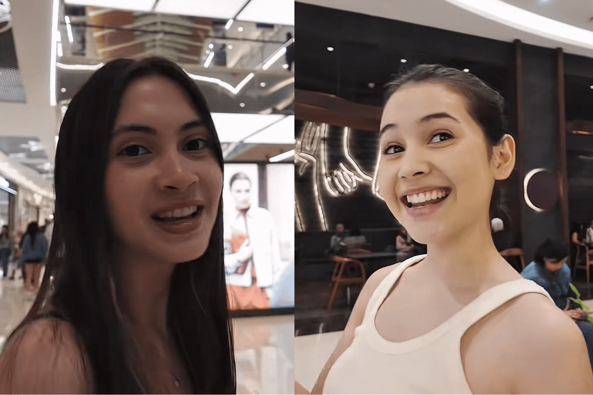 Dua perempuan muda tersenyum ceria saat hangout di pusat perbelanjaan dengan latar interior modern dan pencahayaan terang.