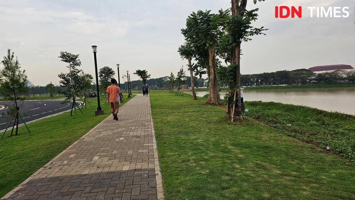Beberapa orang berjalan dan jogging di jalur pedestrian tepi Danau Cihuni, dikelilingi pepohonan hijau di Tangerang.