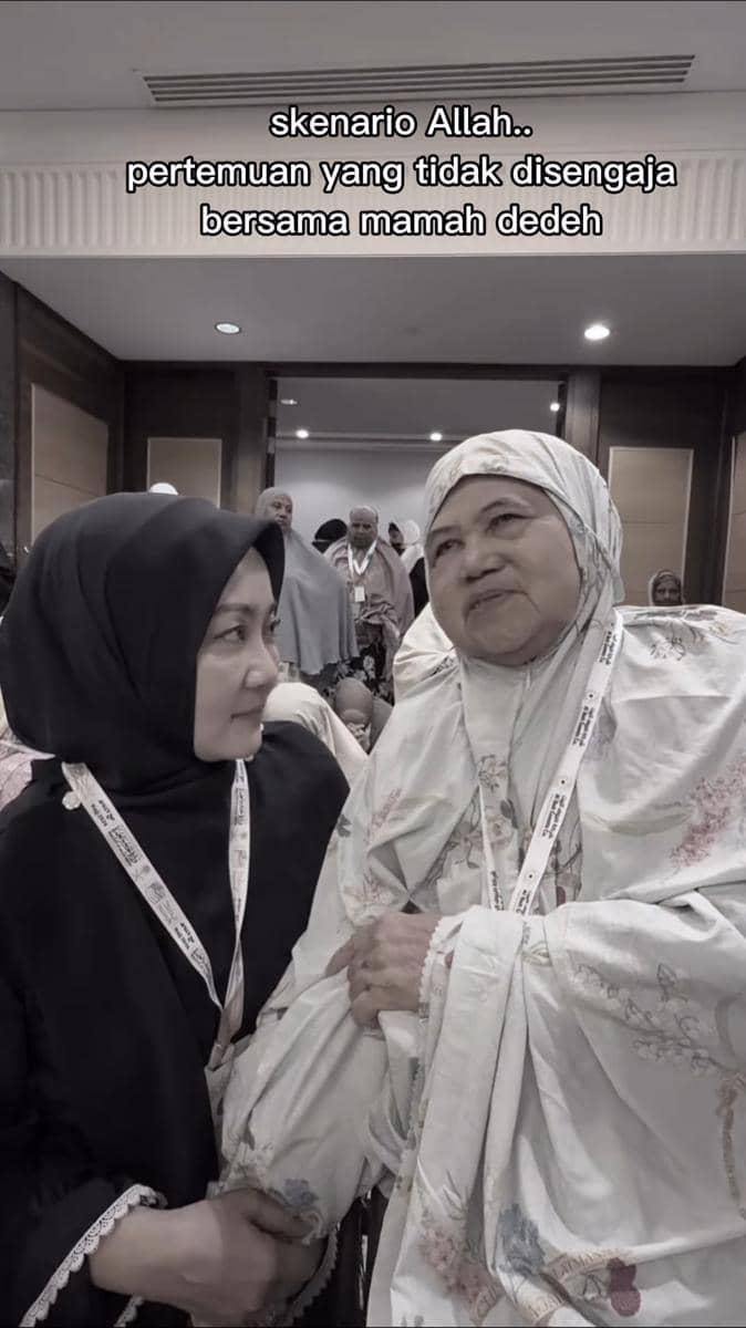 Dua perempuan berhijab saling berbincang hangat di ruang pertemuan saat menjalani ibadah haji, dikelilingi jamaah lain.