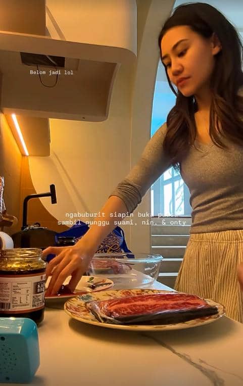 Seorang wanita mengenakan atasan abu-abu sedang menyiapkan makanan di dapur menjelang waktu berbuka puasa Arafah 2026.