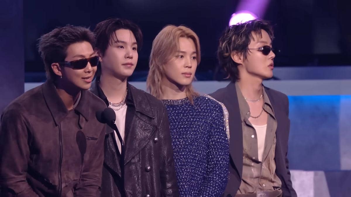 Empat anggota grup musik BTS berdiri di atas panggung American Music Awards 2026 mengenakan busana bergaya modern dan elegan.