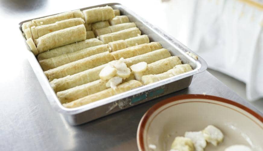 Lontong yang telah matang tersusun rapi di dalam loyang logam dengan beberapa potongan lontong di piring di atas meja dapur.