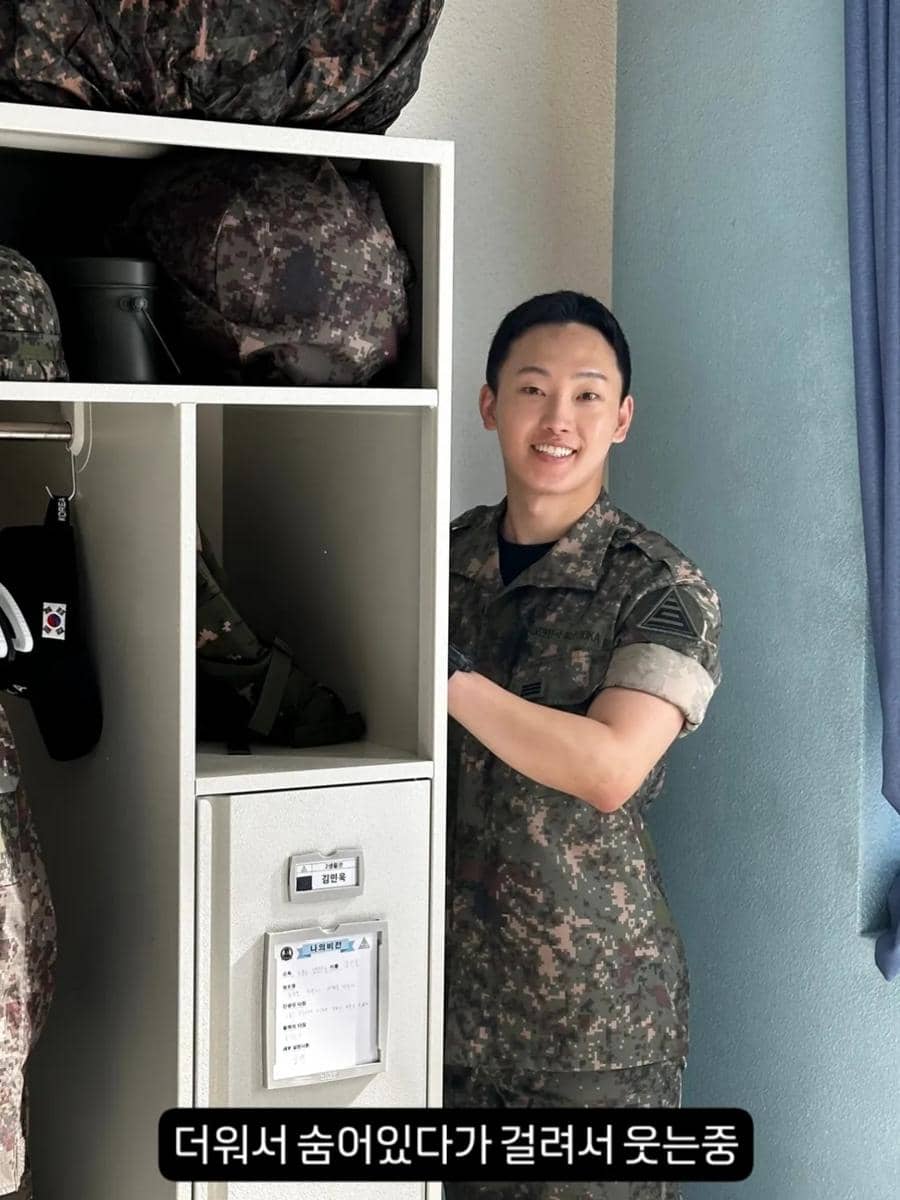 Seorang pria mengenakan seragam militer tersenyum di samping loker perlengkapan tentara di lokasi syuting drama The Legend of Kitchen Soldier.