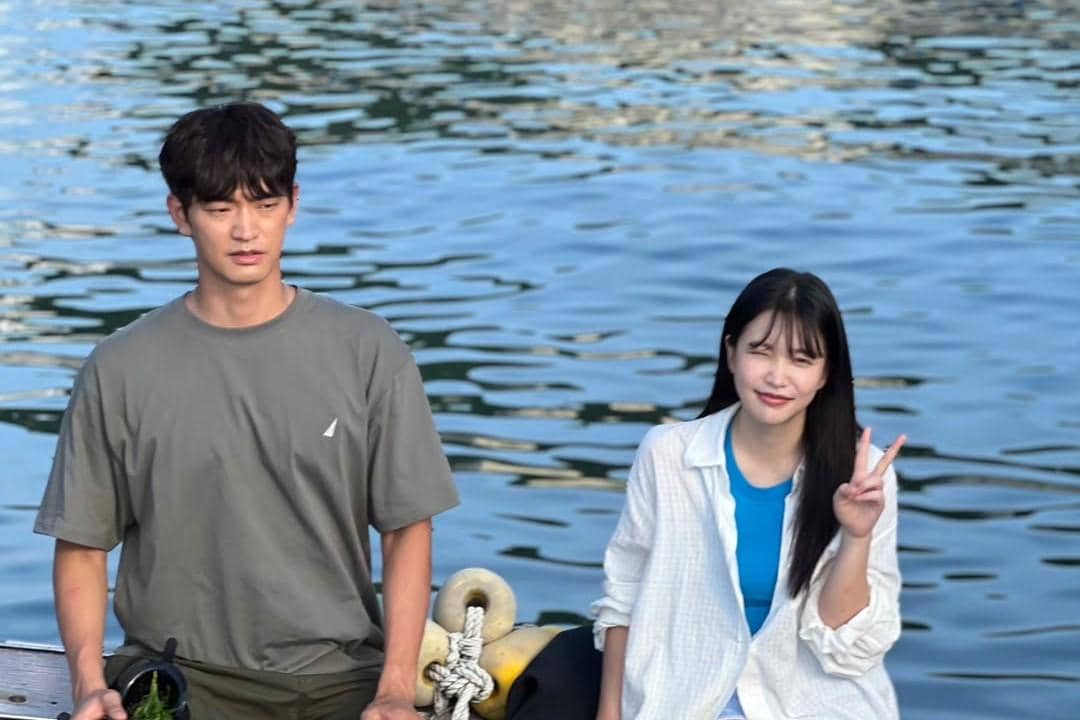 Dua pemeran drama Azure Spring berada di tepi air, satu mengenakan kaus abu-abu dan satu lagi mengenakan kemeja putih sambil berpose damai.