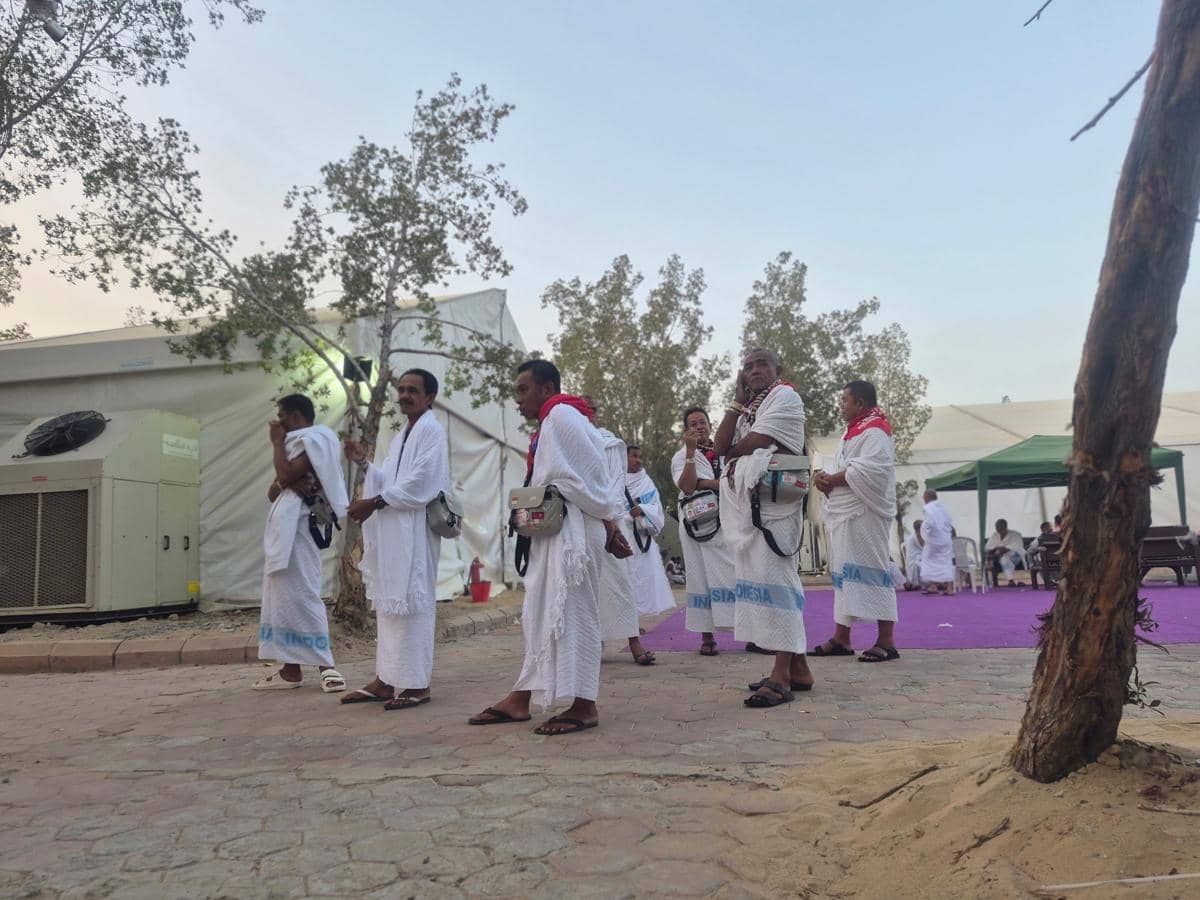 Sejumlah jemaah haji mengenakan pakaian ihram putih menunggu waktu wukuf di area tenda dengan latar pepohonan dan langit sore.
