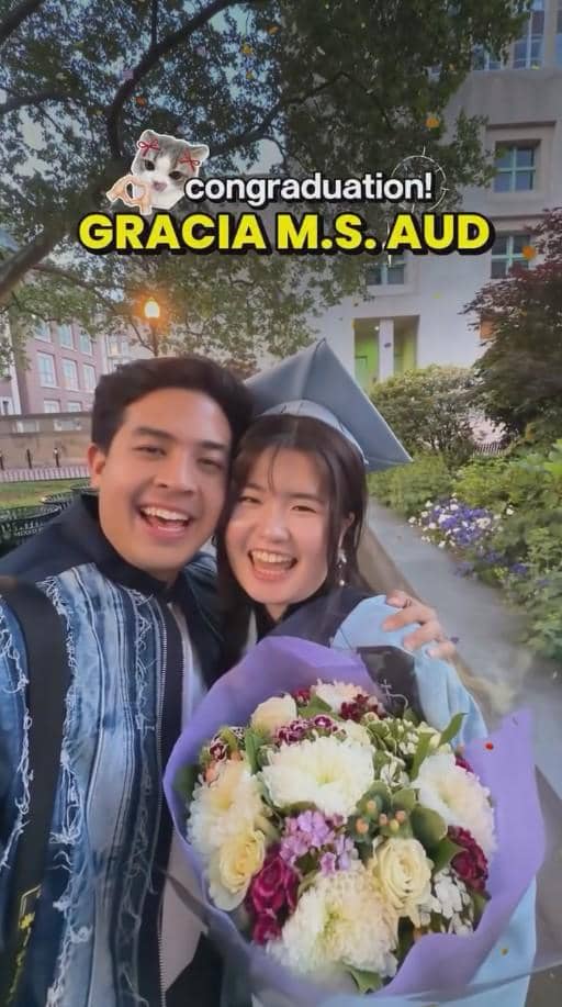 Seorang pria dan wanita tersenyum bahagia sambil berfoto bersama di luar ruangan, wanita mengenakan toga wisuda dan memegang buket bunga berwarna-warni.