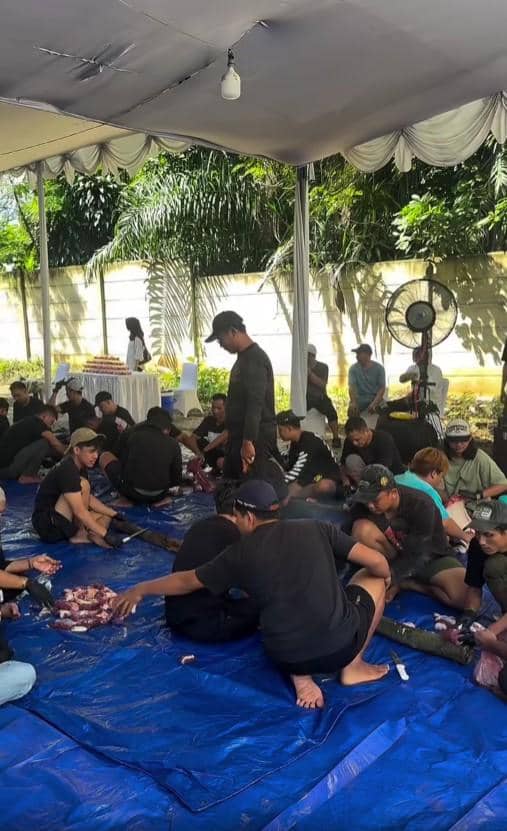 Sejumlah orang duduk di atas terpal biru di bawah tenda, bekerja sama memotong dan mengemas daging kurban saat perayaan Idul Adha.