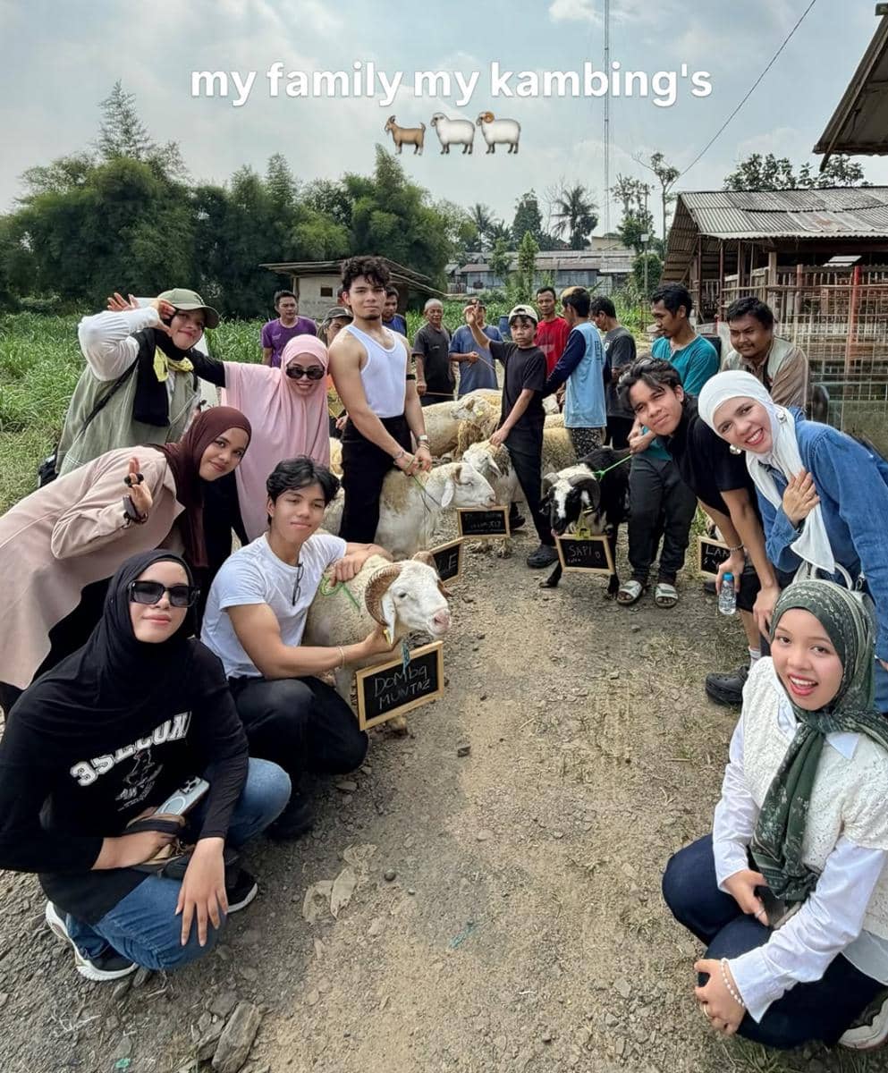Sekelompok orang berpose bersama kambing kurban di area terbuka saat perayaan Idul Adha 2026 dengan latar pepohonan dan kandang.