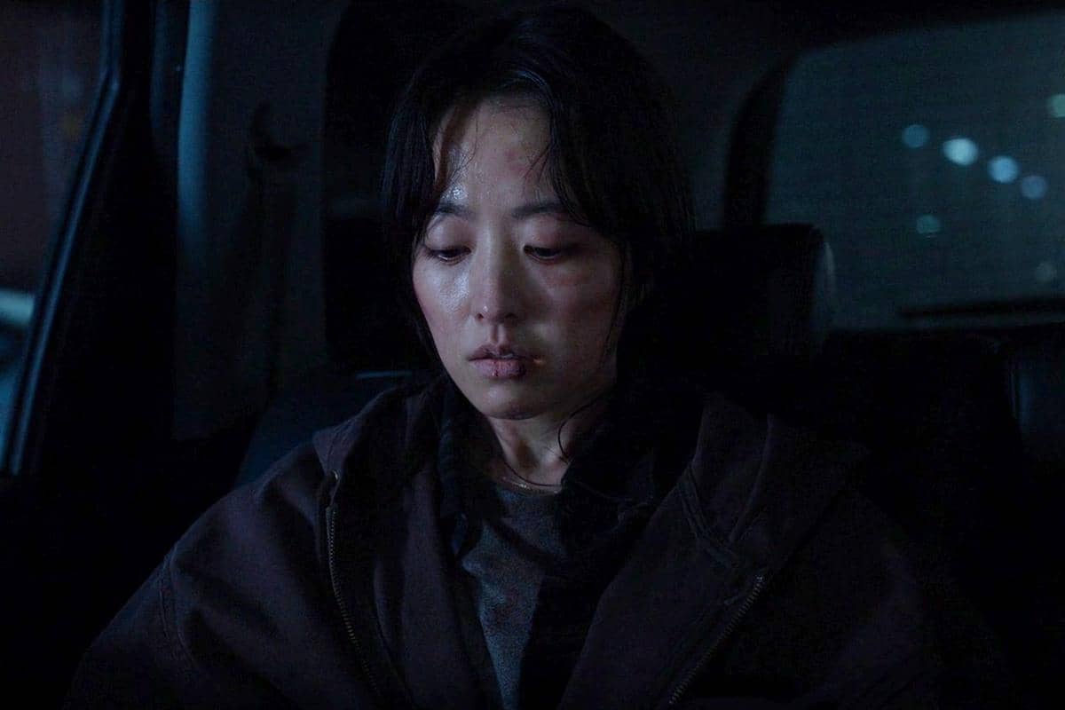 Seorang wanita dengan wajah lelah dan memar duduk di dalam mobil pada suasana gelap dalam adegan drama Korea Gold Land.
