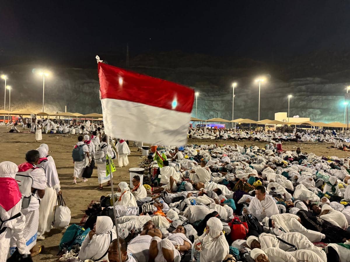Jamaah haji Indonesia bersama jamaah dari berbagai negara beristirahat di Muzdalifah, Makkah, dengan bendera Merah Putih berkibar di malam hari.