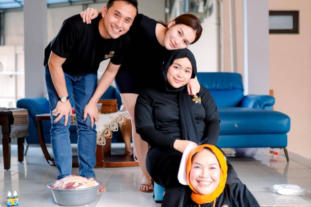 Empat orang berpakaian hitam tersenyum bersama di ruang tamu dengan baskom berisi daging kurban di lantai depan mereka.